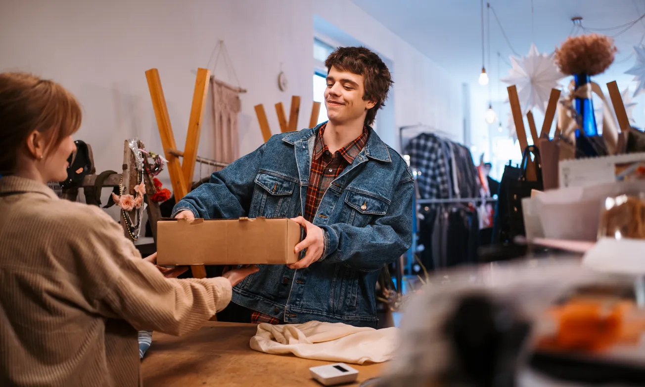 Smiling customer returning a package at a retail store counter, representing in-store returns as part of an omnichannel shopping experience.