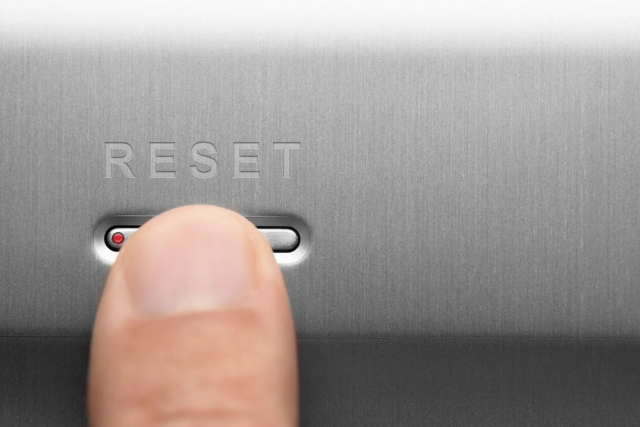 Close-up of a finger pressing a metallic reset button, symbolizing restarting, business transformation, or system reboot.