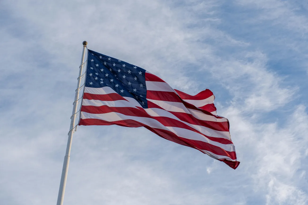 American flag waving against a partly cloudy blue sky.