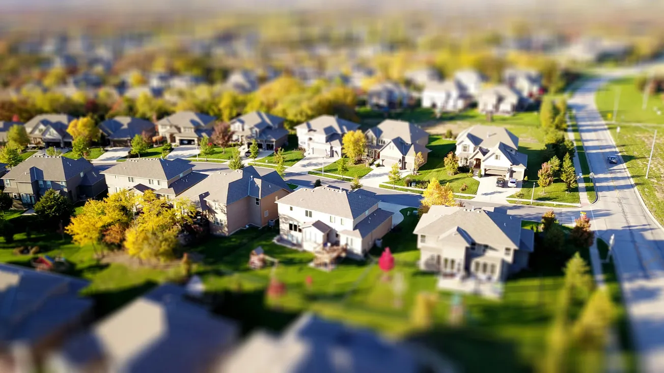 Aerial view of a suburban neighborhood with neatly arranged houses, green lawns, and tree-lined streets on a sunny day.
