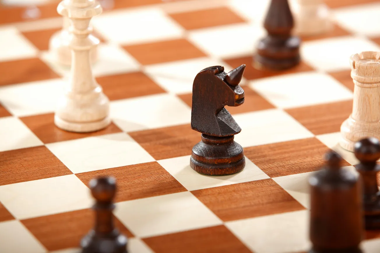 Chessboard close-up with dark wood unicorn knight surrounded by chess pieces. 