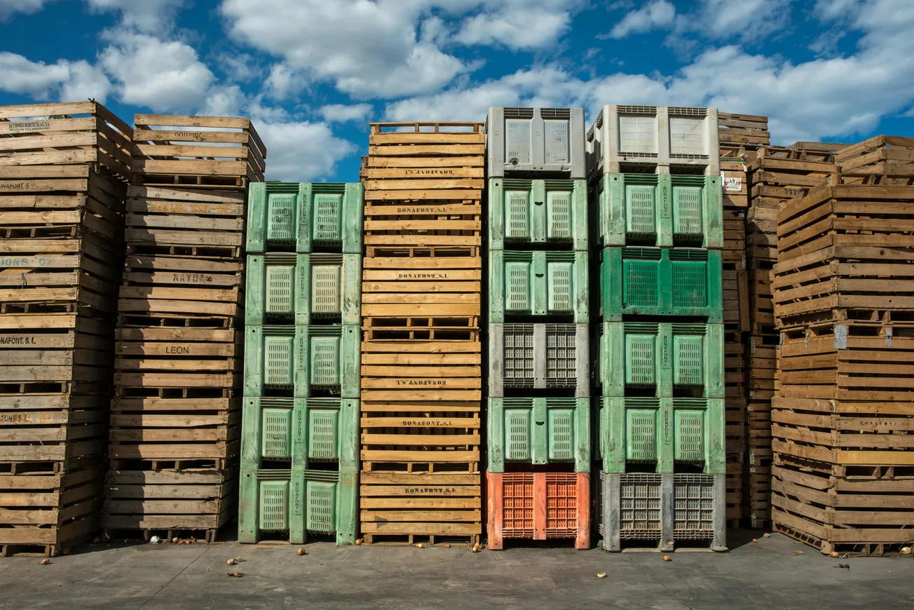 Stacks of wooden and plastic crates arranged outdoors under a blue sky with clouds.
