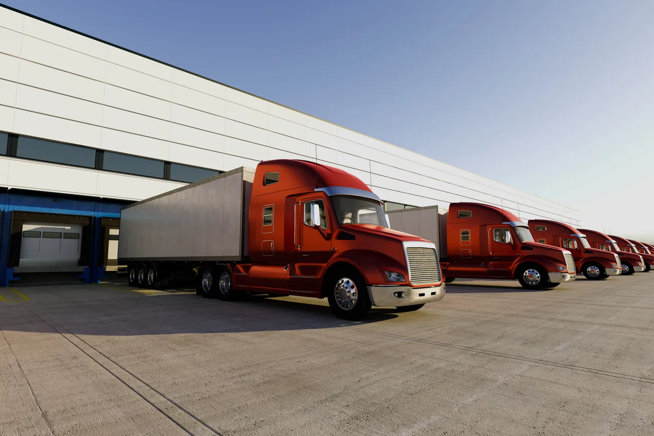 Red semi-trucks lined up in front of a modern warehouse under a clear blue sky, conveying an organized, industrious atmosphere.