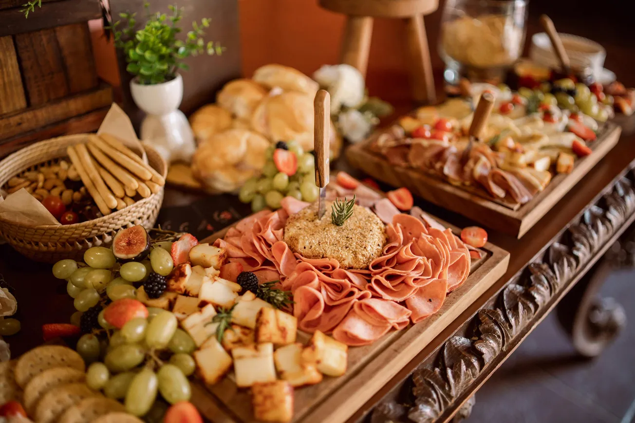 Wooden table with a charcuterie spread including grapes, cheese, meats, and breadsticks.