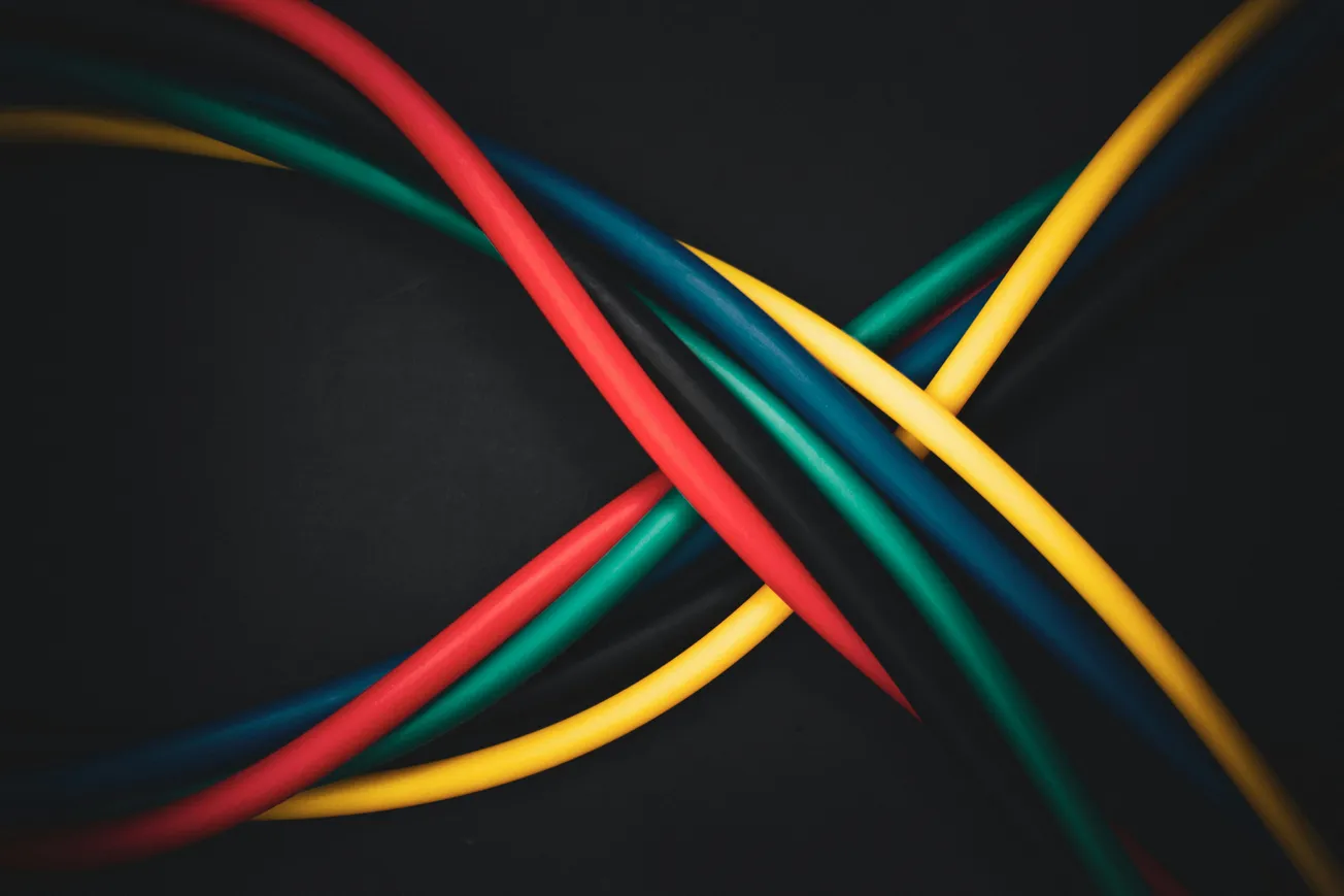 Multicolored cables, including red, yellow, blue, green, and black, intersect on a black background, creating an abstract, dynamic pattern.