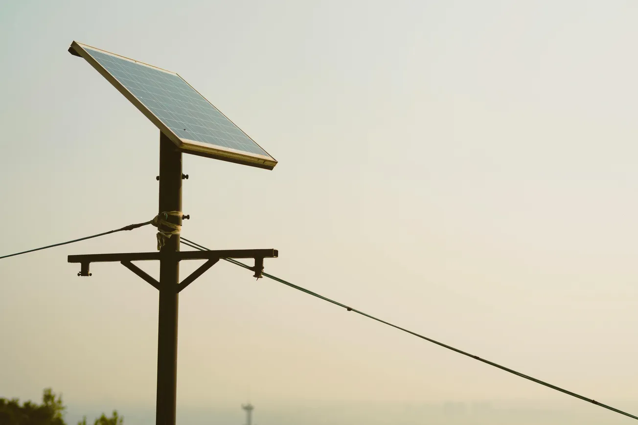 A single solar panel mounted on a pole against a hazy sky, with wires extending diagonally.