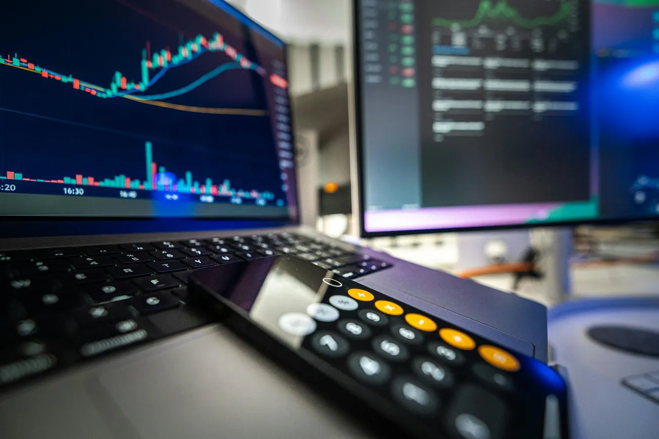 A laptop displaying a stock chart with colorful graphs, beside a calculator app on a smartphone.