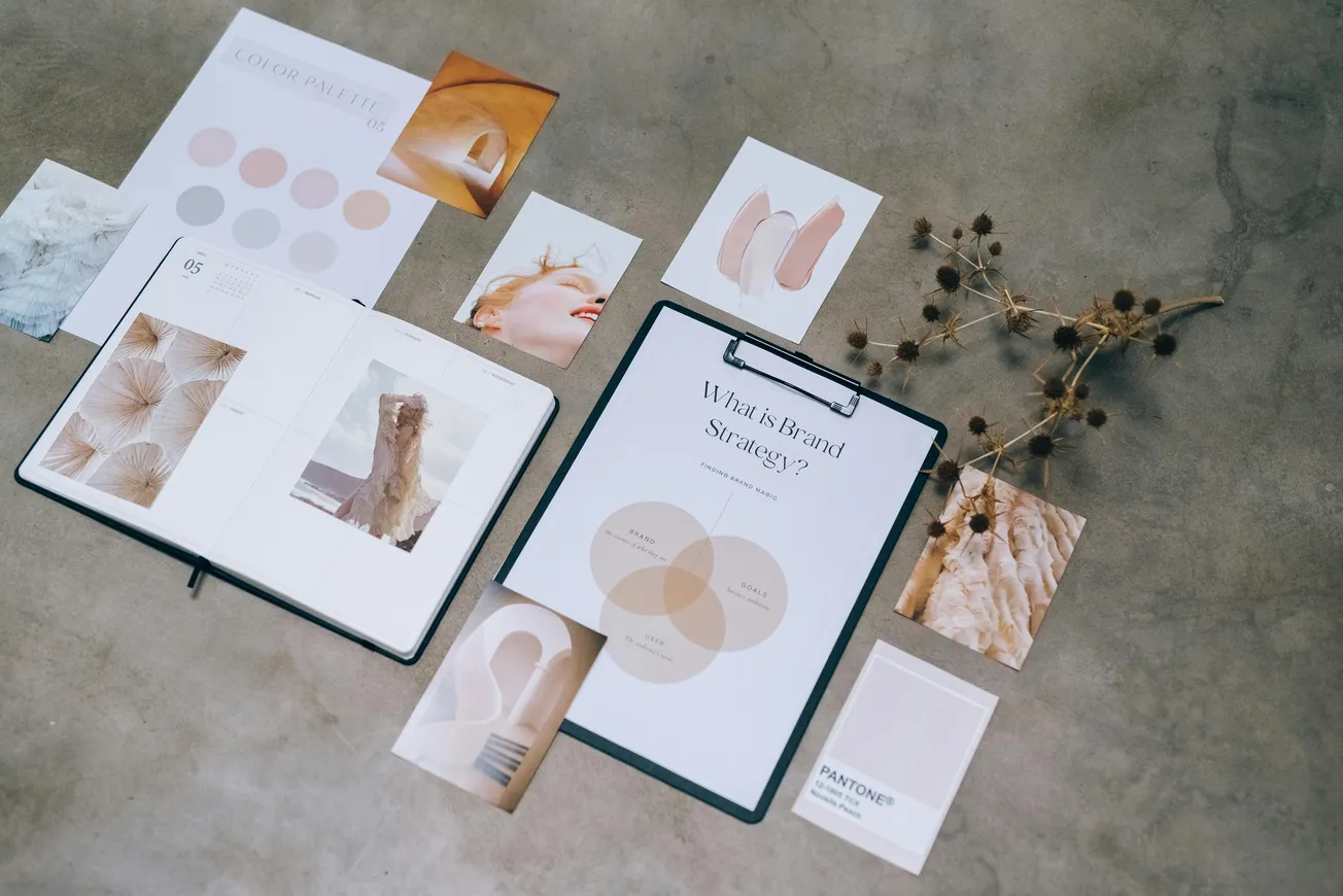 A collection of design elements on a gray background, featuring an open book, color palette, branding strategy chart, photos, and dried flowers.