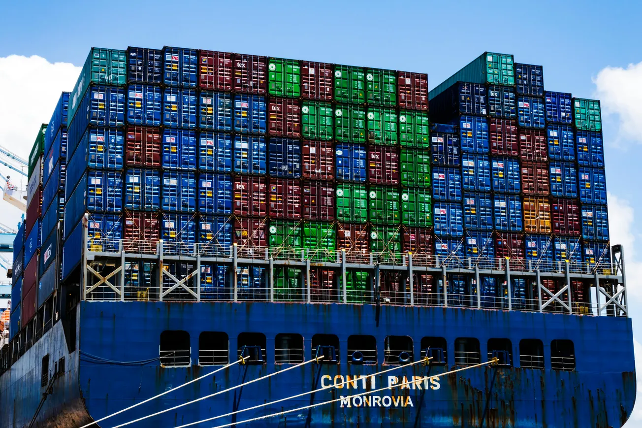 Cargo ship Conti Paris stacked with colorful shipping containers docked at port under blue sky.