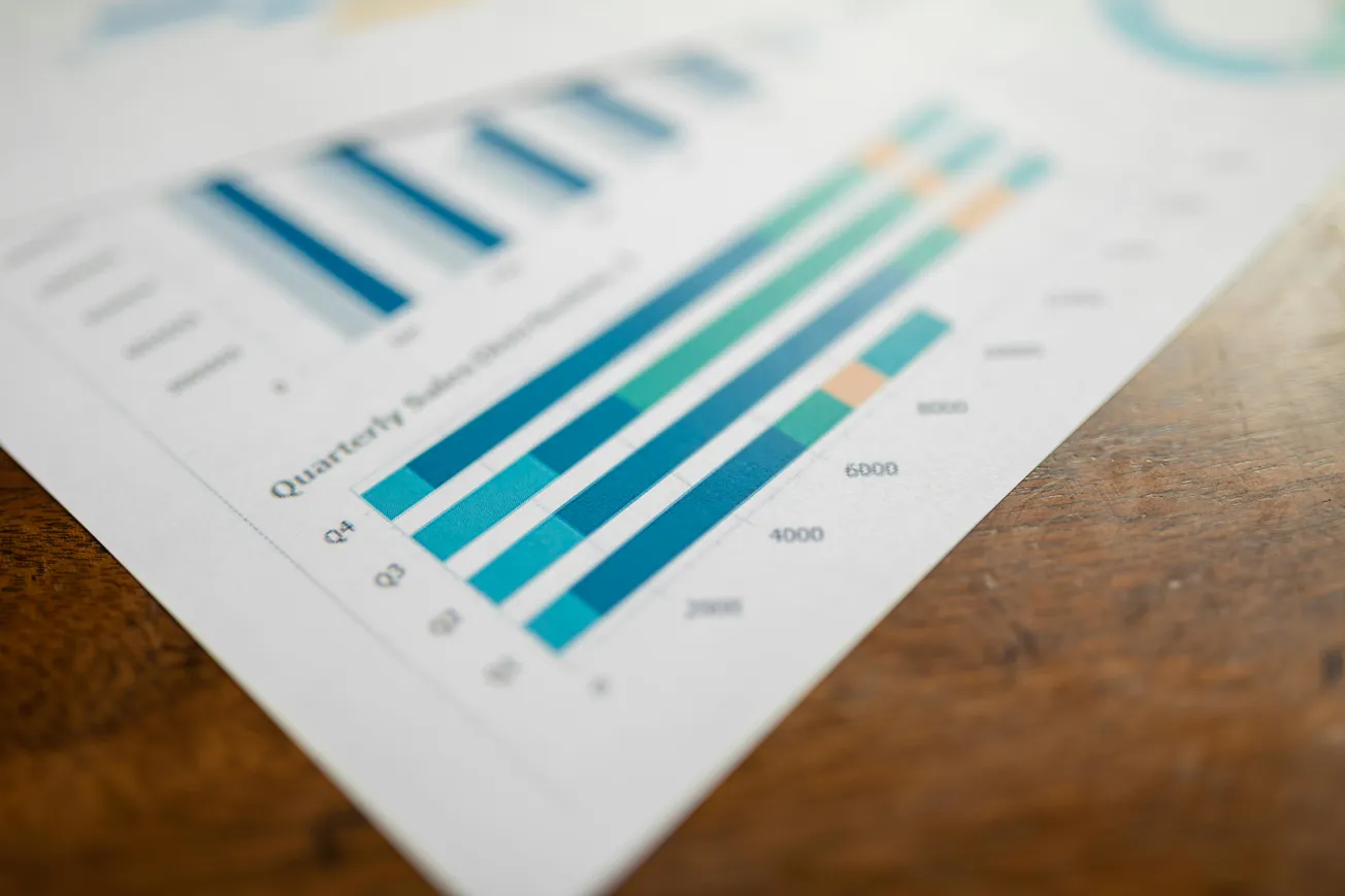 Close-up of a document with colorful bar graphs displaying quarterly sales performance, on a wooden table.
