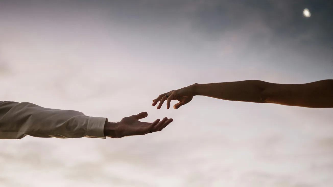 Two hands reaching towards each other against a twilight sky.