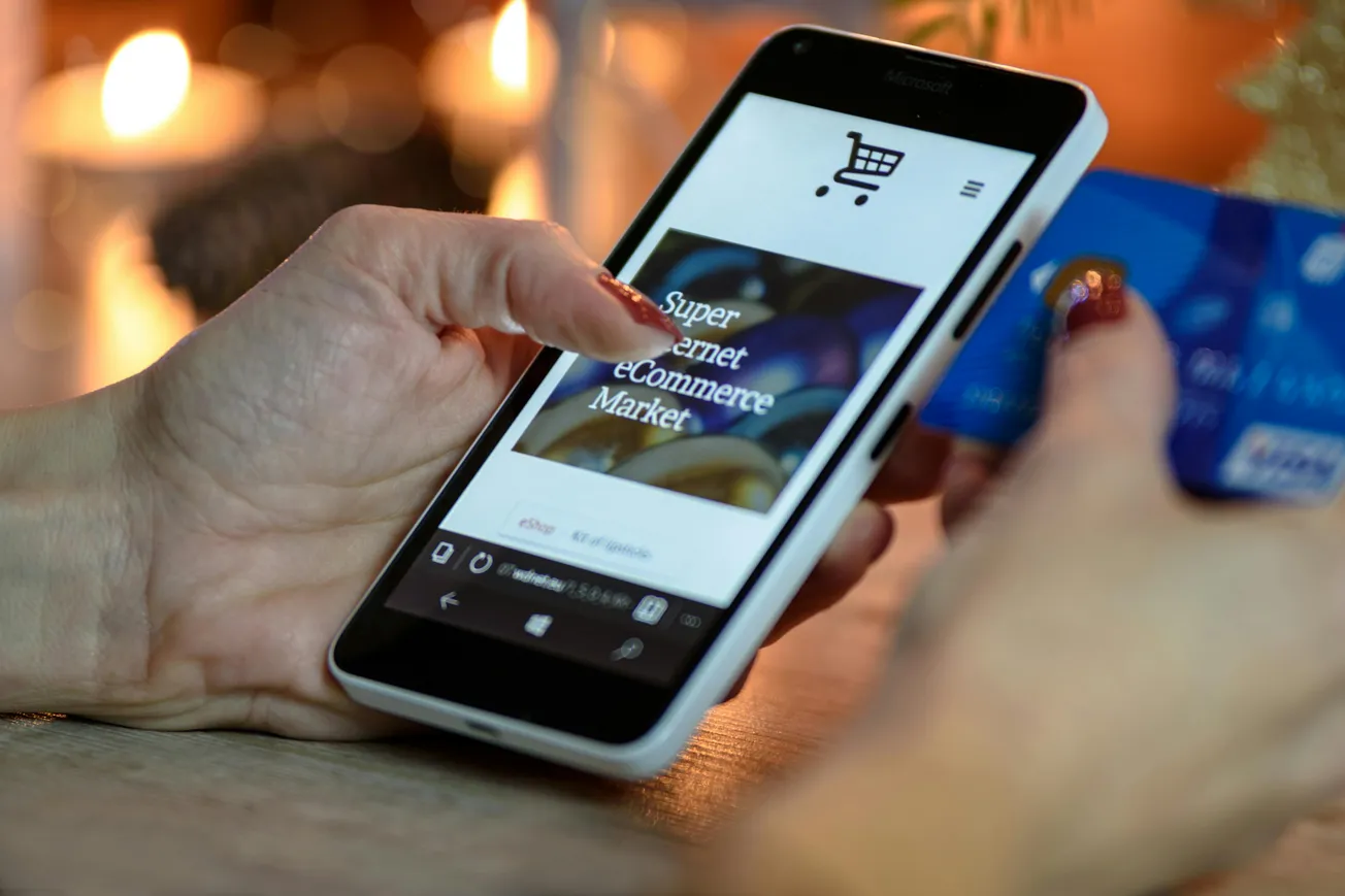 A person shops online with a smartphone and holds a credit card. The phone screen displays an eCommerce site.