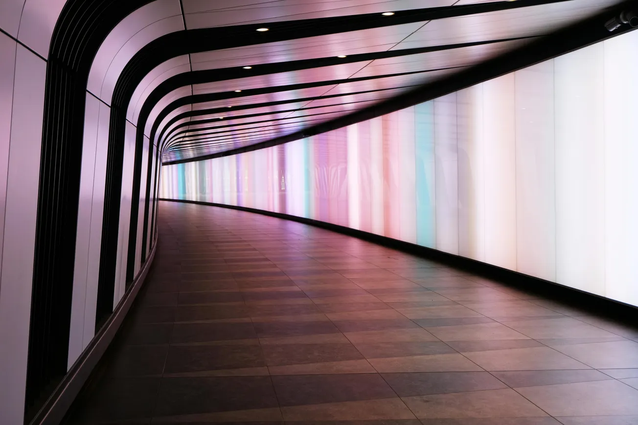 Curved tunnel with illuminated walls in pastel hues, including pink, purple, and blue. The sleek, modern design creates a futuristic ambiance.