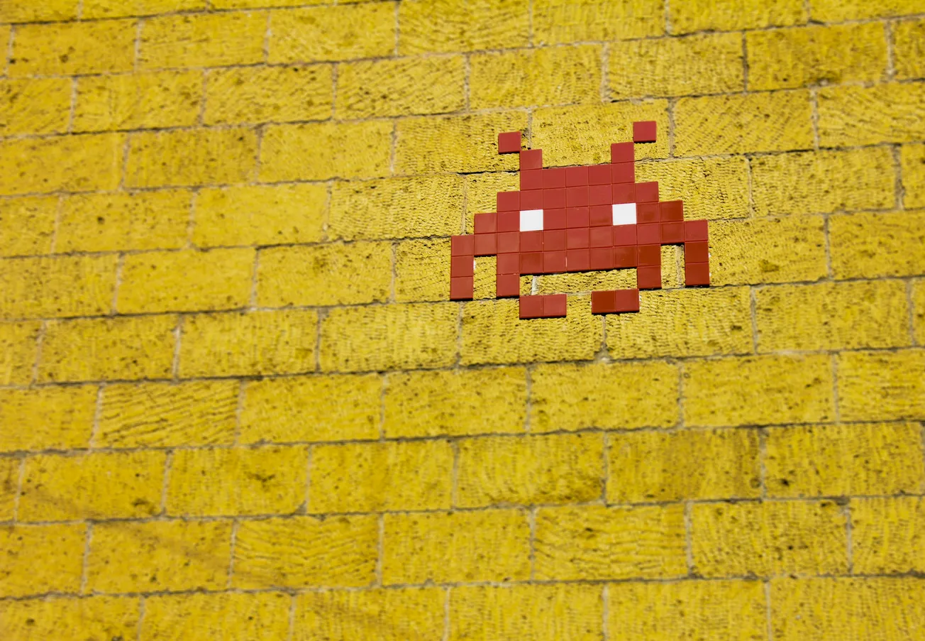 Pixelated red alien from classic video games on a textured yellow brick wall, evoking a nostalgic and playful tone.