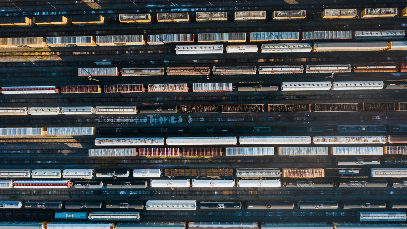 Aerial view of a railway yard filled with parallel rows of stationary train cars. The image captures an orderly pattern, evoking a sense of industrial calm.