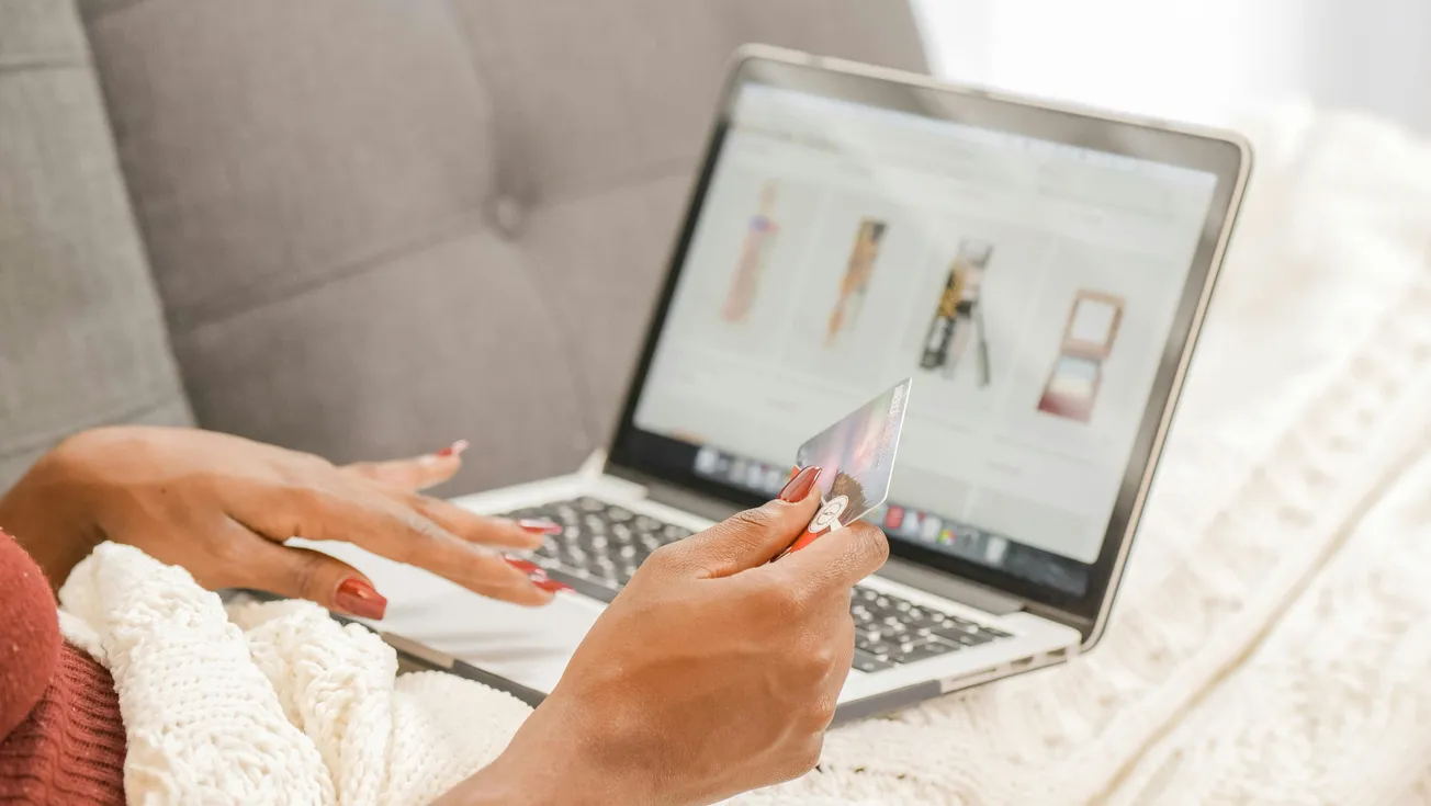 A person holds a credit card while online shopping on a laptop, browsing beauty products.