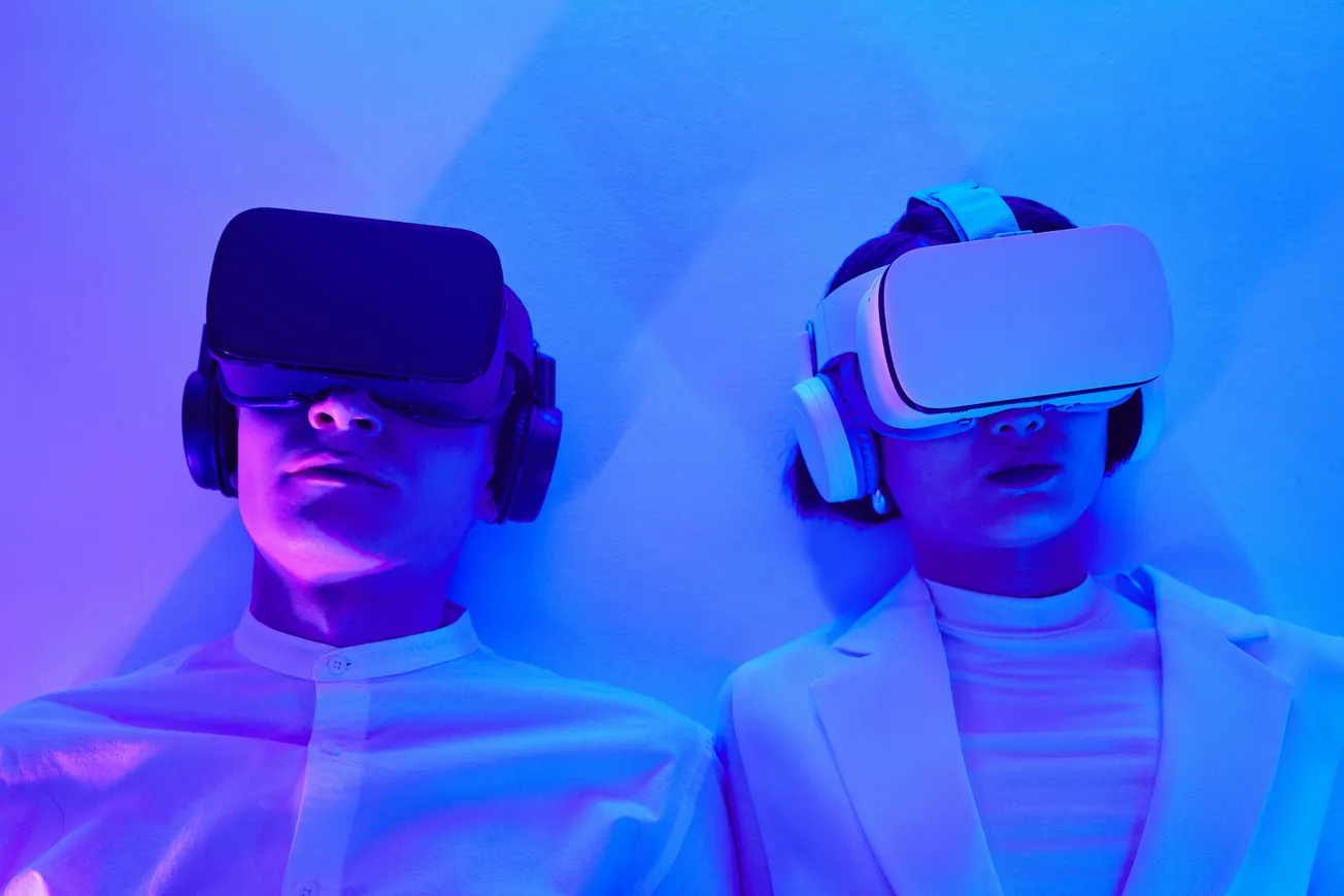 Two individuals wearing virtual reality headsets lie against a wall, illuminated by blue and purple light.