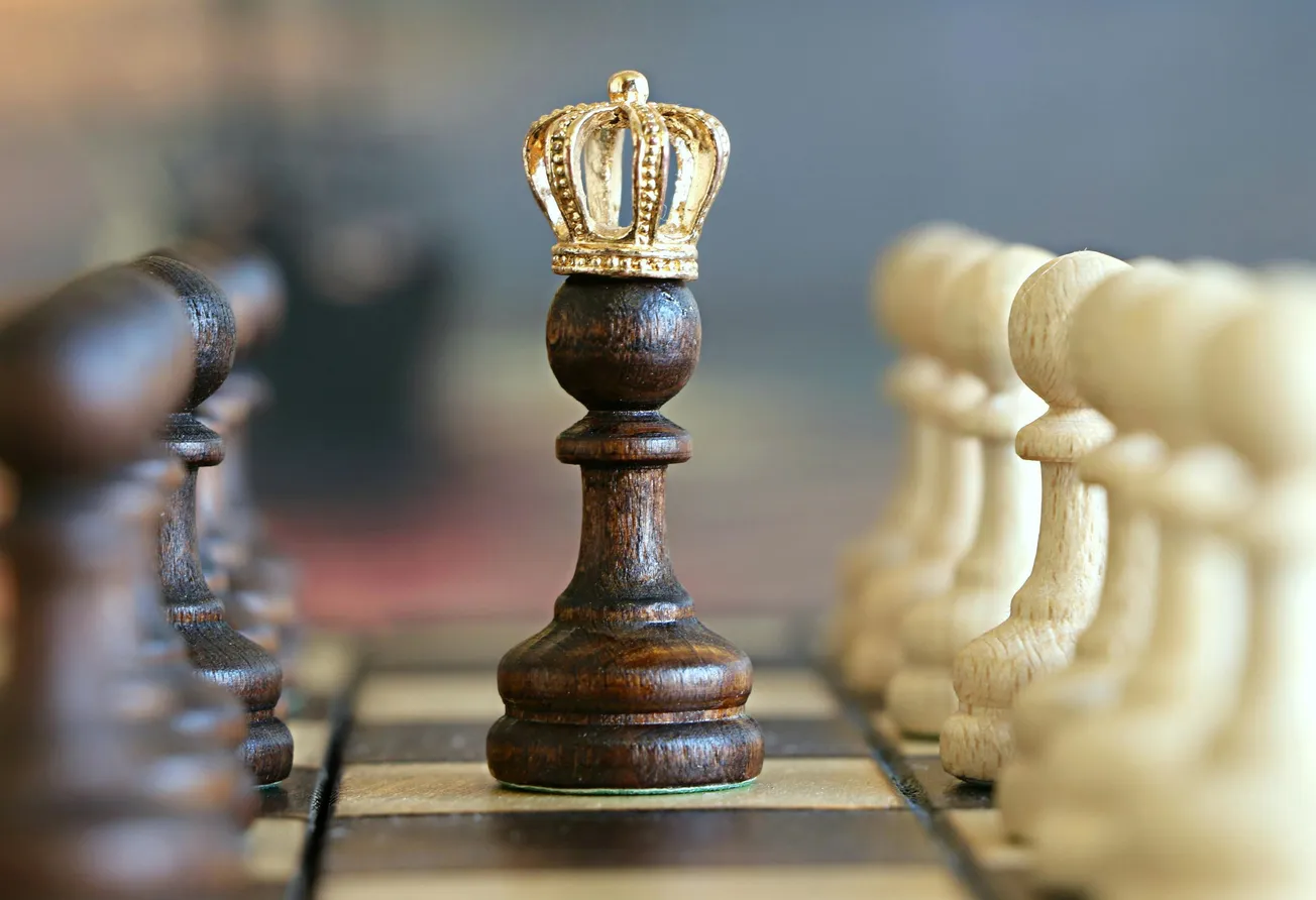 A dark chess pawn with a golden crown on top is centered on a chessboard, symbolizing power. Surrounding white pawns highlight its prominence.