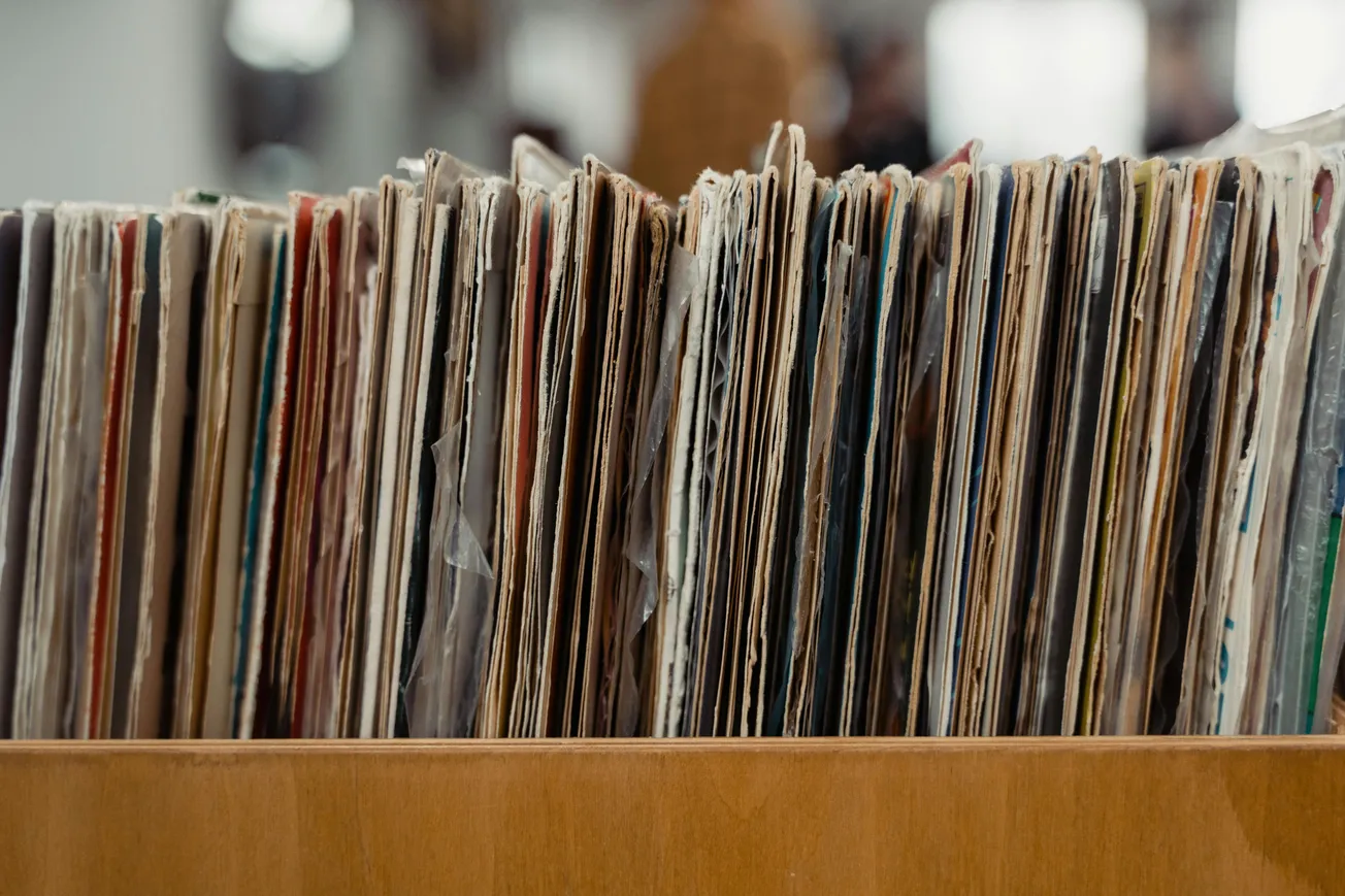 A close-up of a collection of vintage vinyl records in worn sleeves, neatly lined up vertically in a wooden crate, evoking nostalgia and timeless appeal.