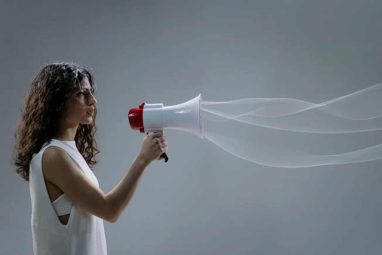 A woman in a white sleeveless top holds a megaphone, with translucent sound waves emanating. The background is gray, conveying a sense of communication.