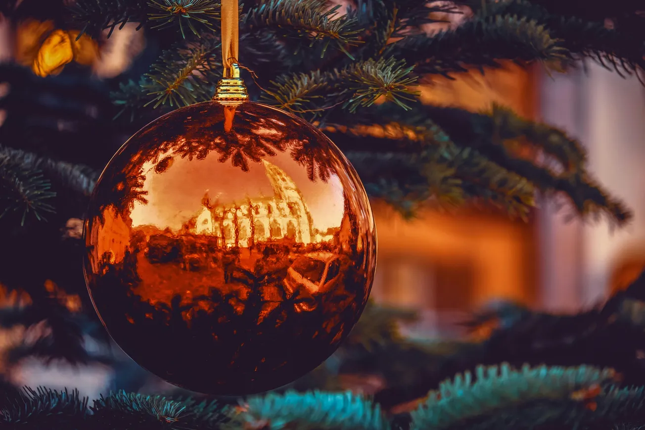 Close-up of a reflective orange Christmas ornament on a tree, with a scenic reflection of a building and warm golden light, evoking a festive atmosphere.
