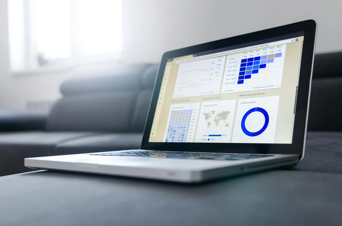 Open laptop on a sofa displays graphs and charts, including line graphs and pie charts, against a bright background, conveying data analysis.