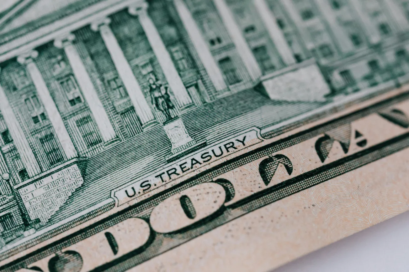 Close-up of a U.S. ten-dollar bill focusing on details of the U.S. Treasury building, with visible columns and architectural elements in green and beige tones.