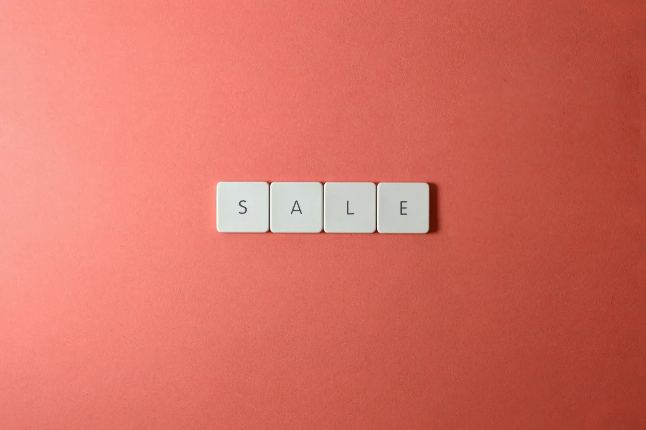 White tiles spelling "SALE" on a coral background. The minimalist design conveys simplicity and draws attention to the message.