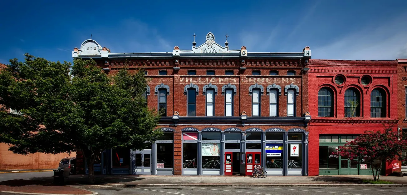A historic brick building with ornate details, tree in front, clear blue sky. Emphasizes vintage architecture and small-town charm, with bicycles leaning on the facade.