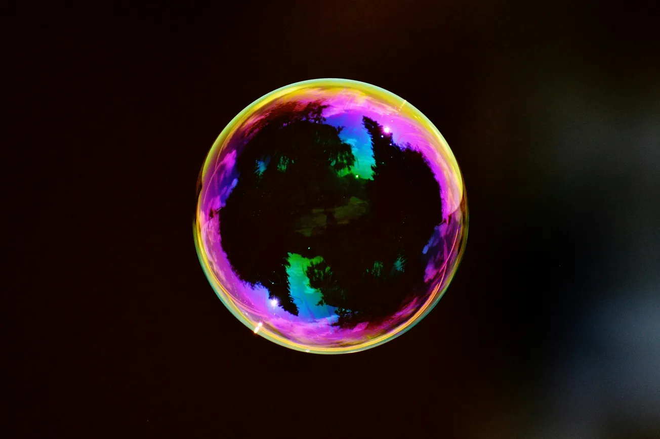 A single soap bubble against a dark background, displaying vibrant rainbow colors with swirling patterns and a reflective surface, creating a whimsical feel.