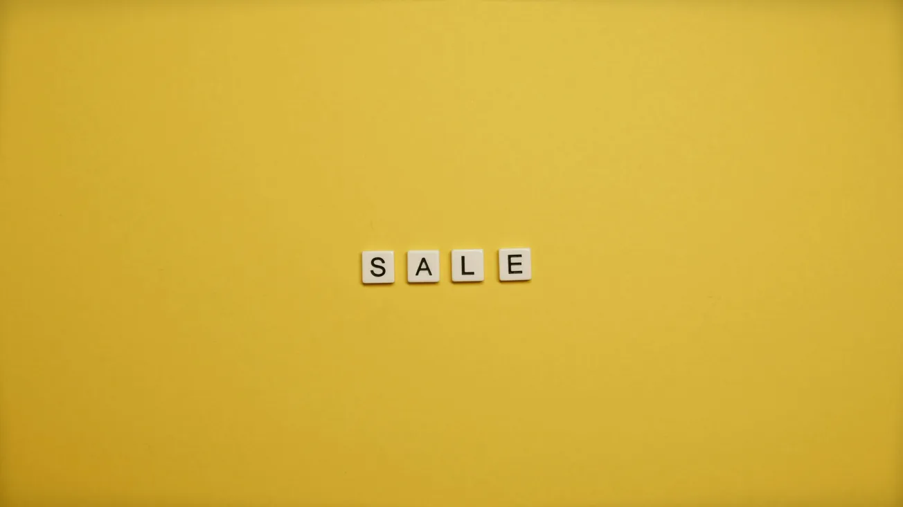 Yellow background with the word "SALE" in white Scrabble-like tiles centered. The minimalist design conveys a bright, cheerful promotion.