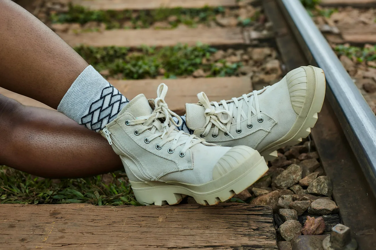 Person wearing beige high-top sneakers with rugged soles and geometric-patterned socks, sitting on a railway track. The scene feels relaxed and adventurous.