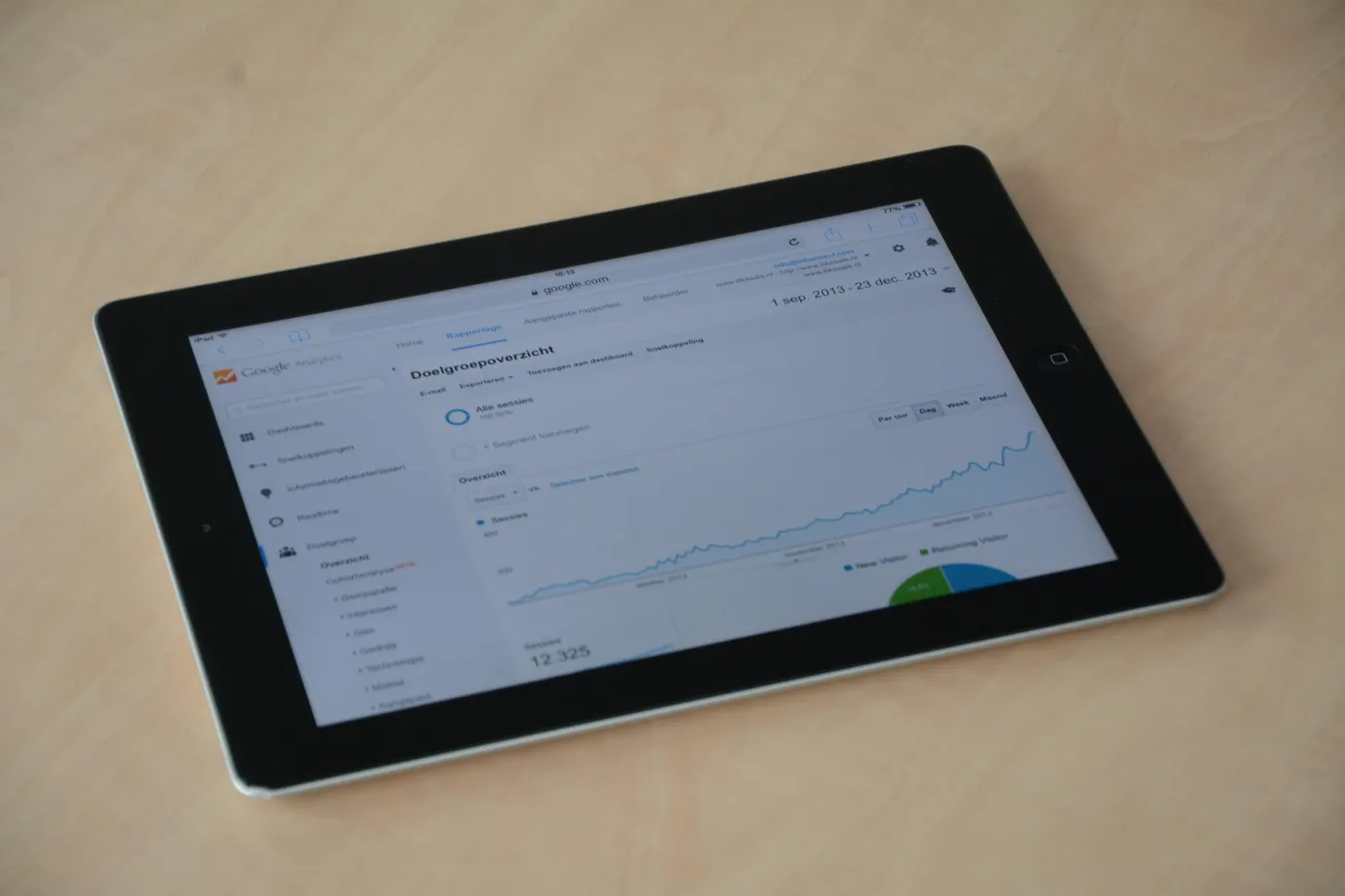 Tablet displaying Google Analytics on a light wood surface. The screen shows a graph trending upward, suggesting growth in data or metrics.