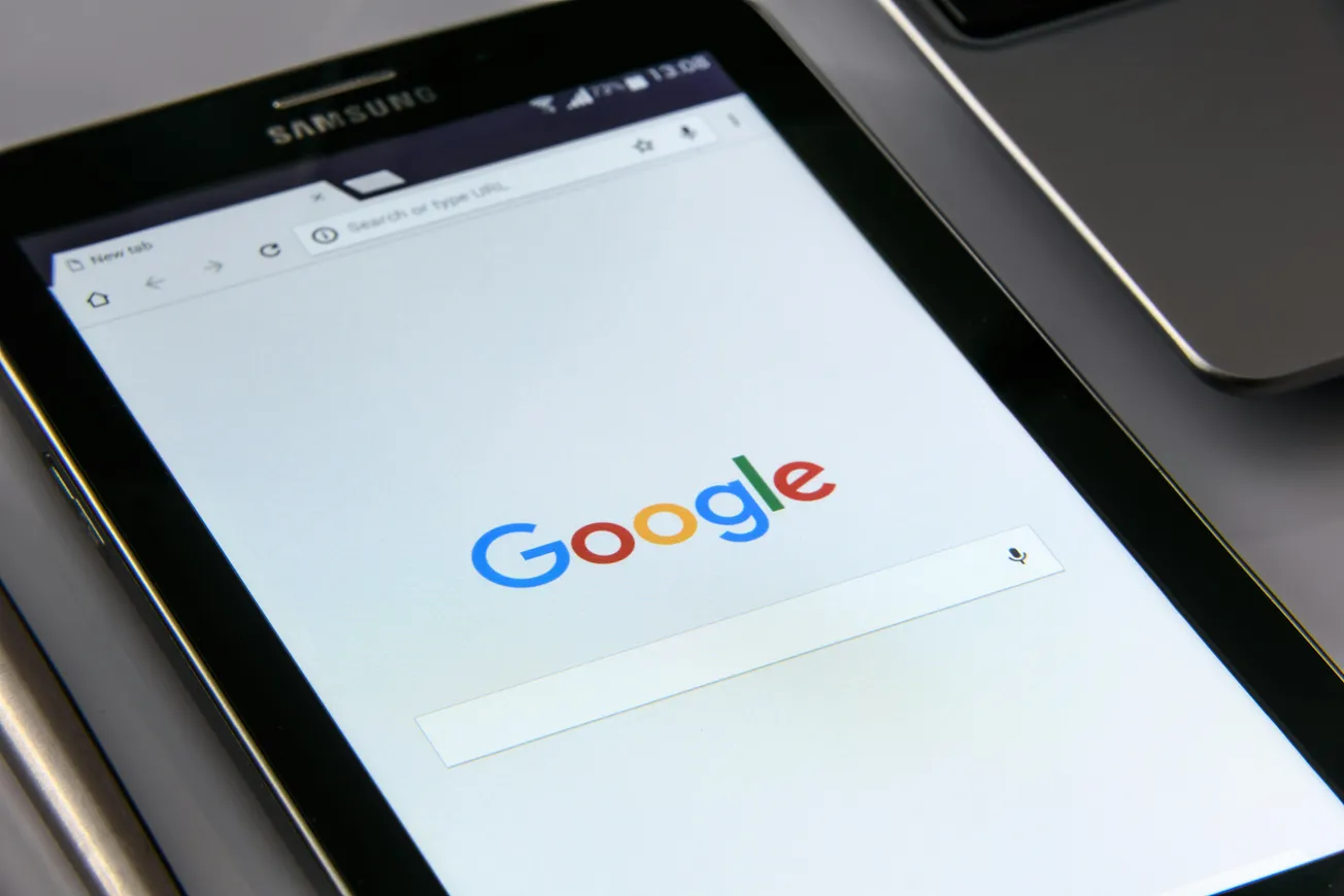 A tablet displaying the Google homepage is angled beside a laptop. The screen shows Google's logo above the search bar, conveying a sense of online connectivity.