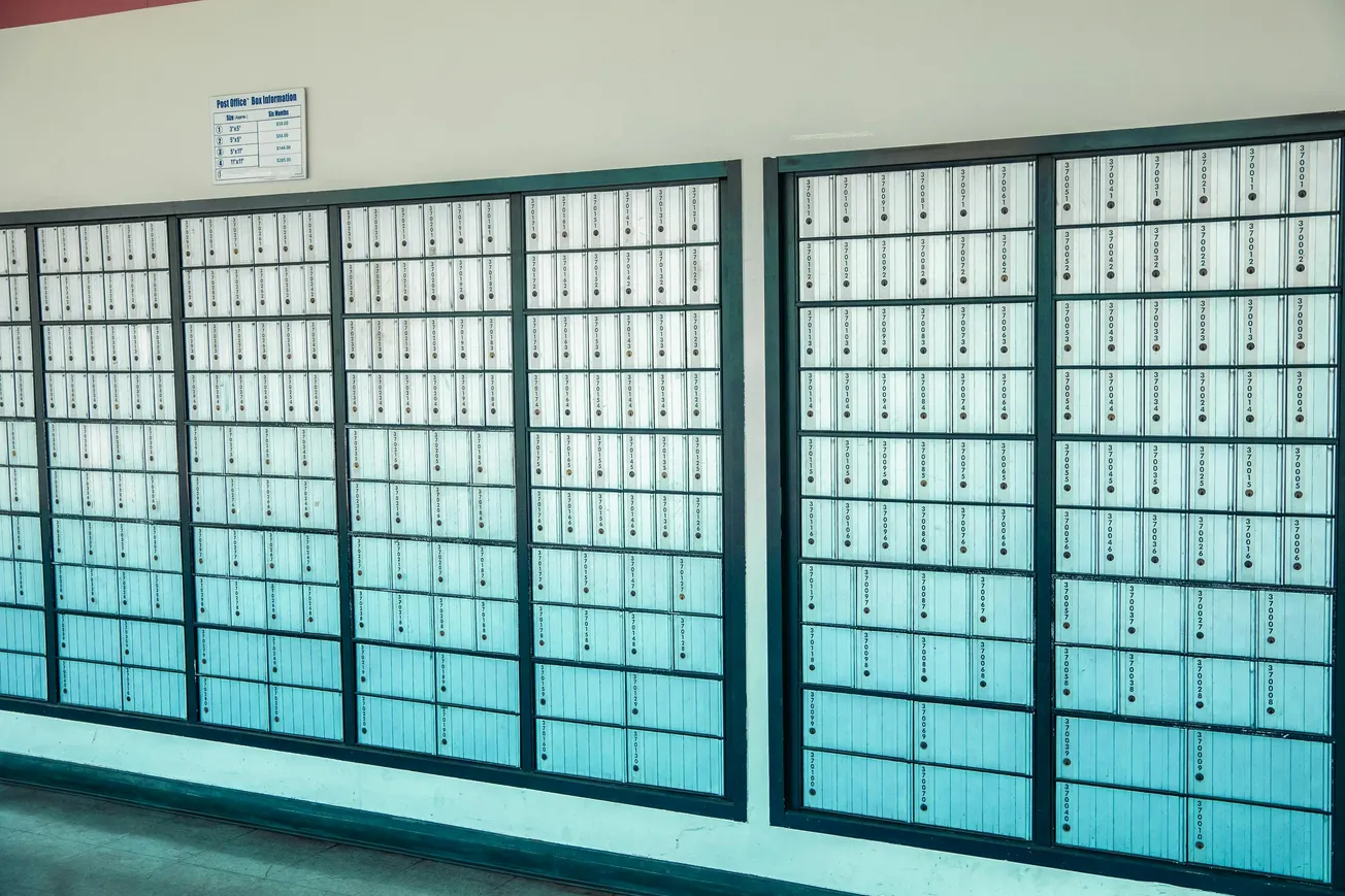 A wall of post office boxes fills the image, each with a small lock and label. The tone is orderly and institutional, conveying efficiency.