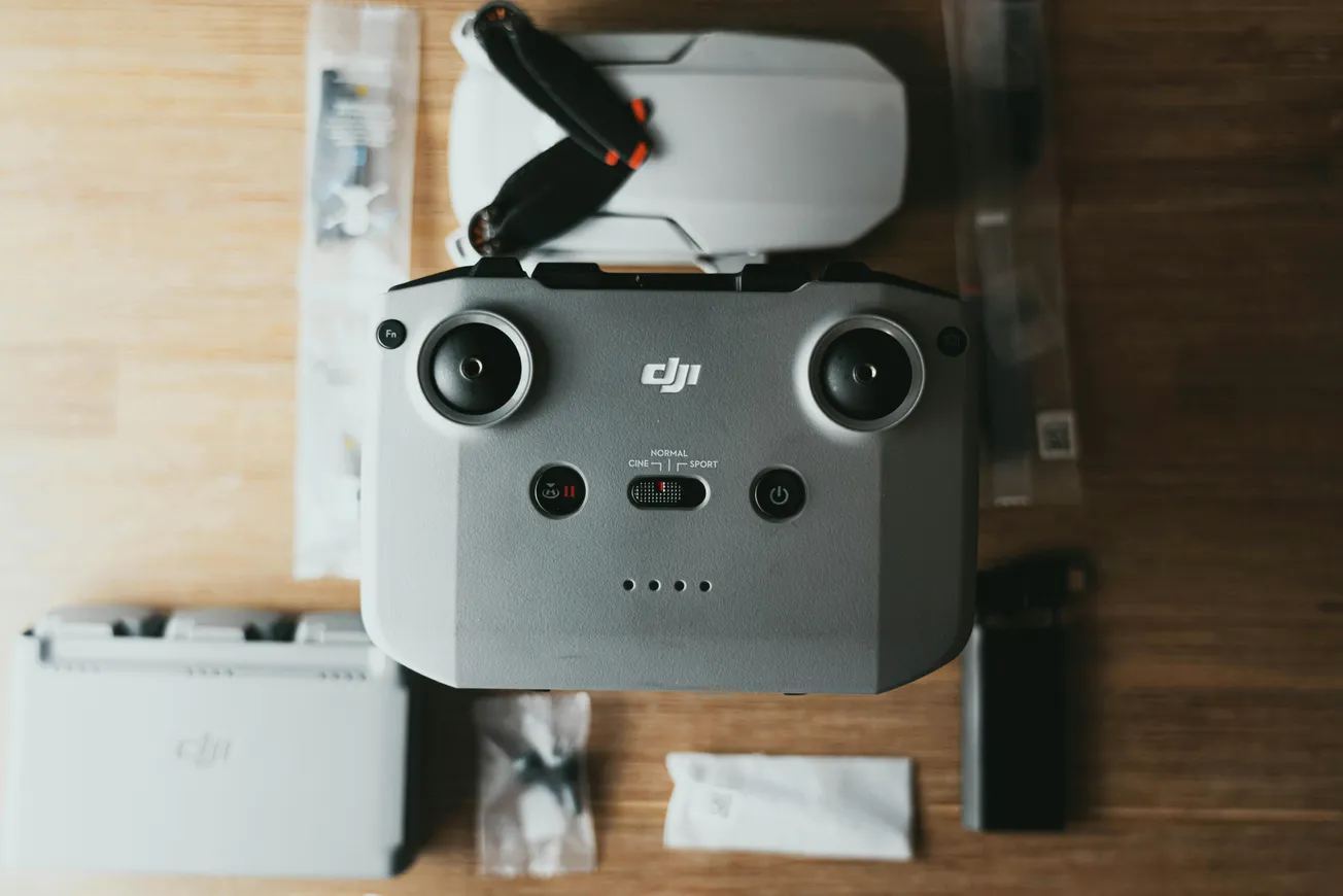 Drone controller with joysticks in focus on wooden surface, surrounded by drone parts and accessories. Neutral tones create a tech-efficient vibe.