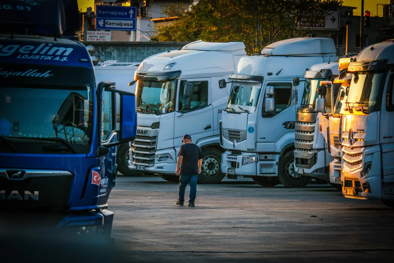 A man in a cap walks through a parking lot filled with rows of white trucks at sunset. The scene conveys a sense of industry and calm.