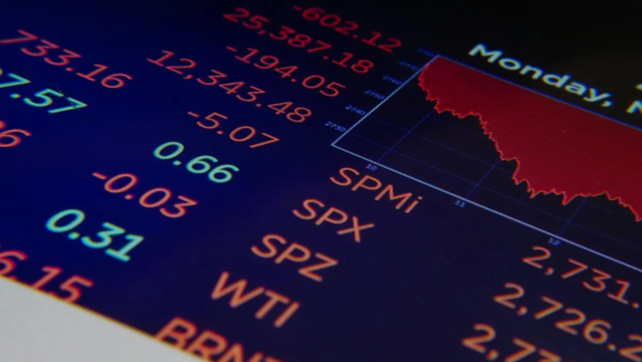 Screen displaying a financial market graph in red indicating a downturn, surrounded by numbers and codes on a dark background, conveying a negative financial tone.
