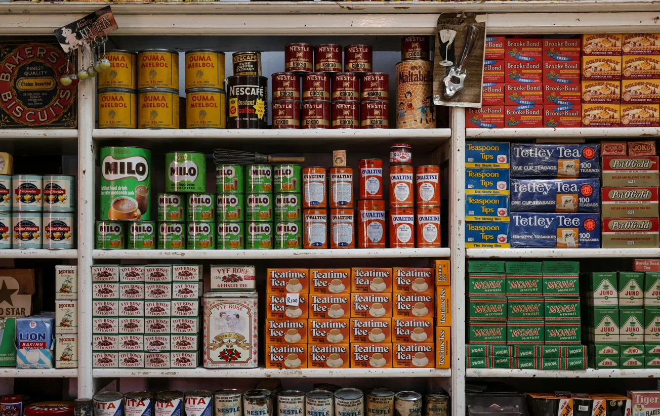 Shelves stocked with vintage tins and boxes of Milo, Nescafé, and various teas. A nostalgic display evoking a sense of an old-fashioned grocery.