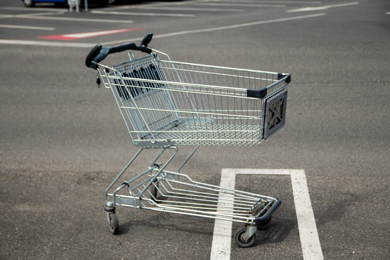 A metal shopping cart in an empty parking lot, positioned neatly in a designated space. The setting is sunny and emphasizes a sense of calm and order.