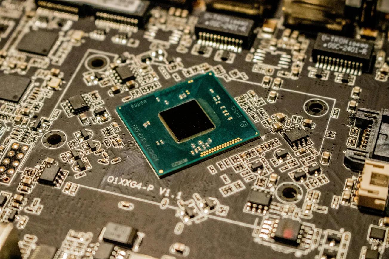 Close-up of a computer motherboard, showcasing a central green processor chip. The circuit board is densely packed with various electronic components.