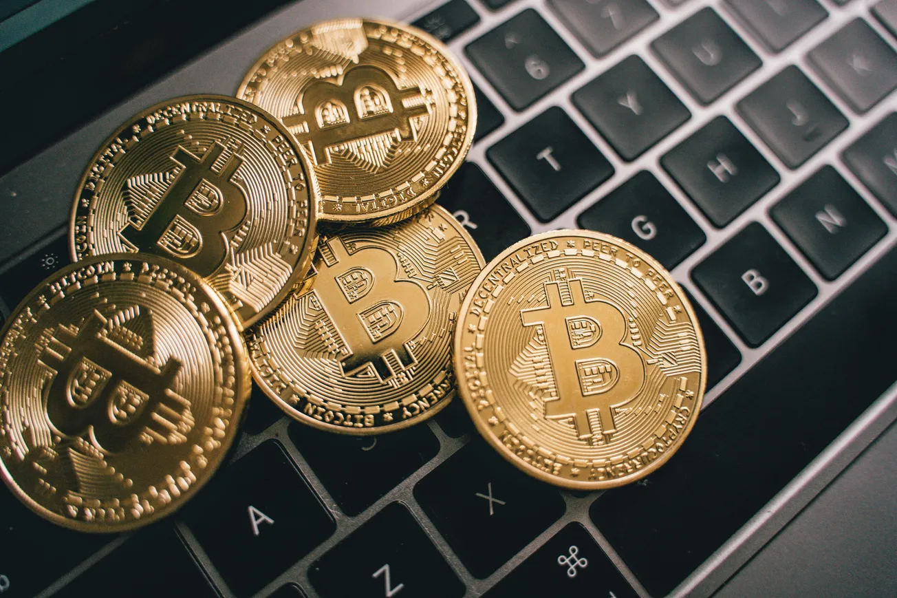 Five gold Bitcoin coins lie scattered on a laptop keyboard. The scene conveys a modern financial theme, highlighting digital currency and technology.