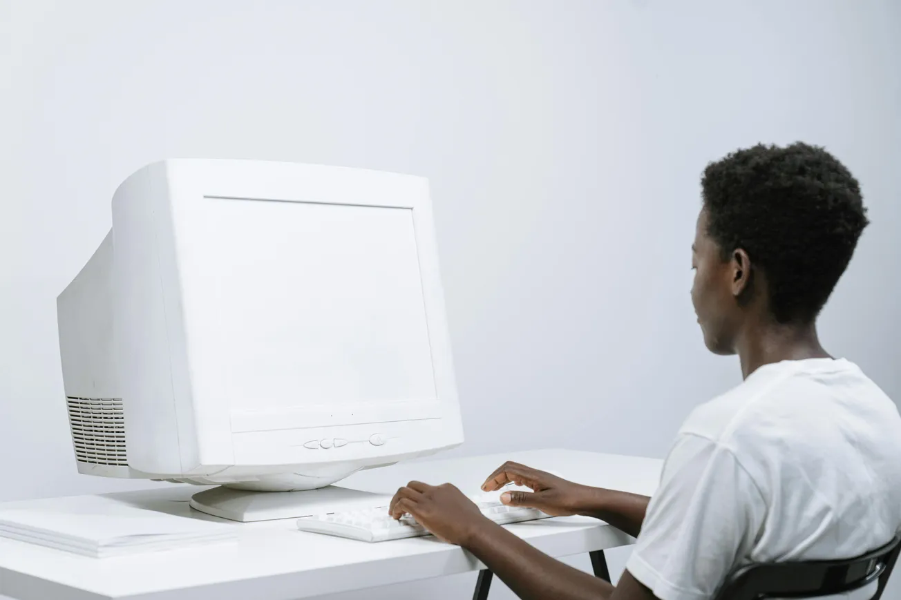 A person in a white T-shirt sits at a desk using a vintage CRT monitor and keyboard, exuding a nostalgic, retro tech vibe in a minimalist setting.
