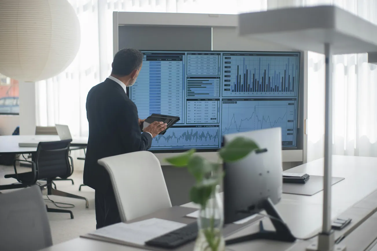 A man in a suit analyzes financial data on large screens in a modern office, conveying a professional and focused atmosphere.