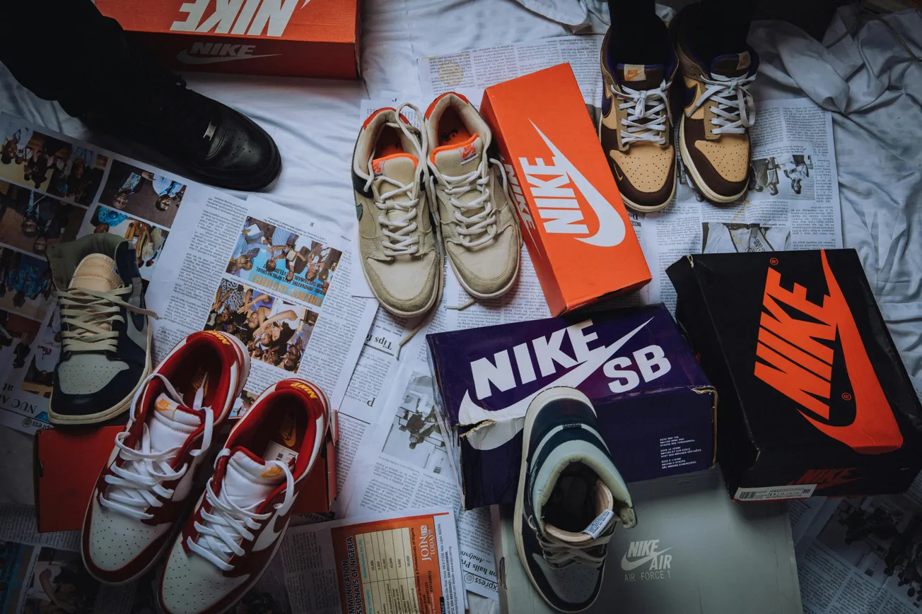 A collection of Nike sneakers is displayed on a sheet-covered floor with open boxes and various styles, evoking a sense of sneakerhead enthusiasm.