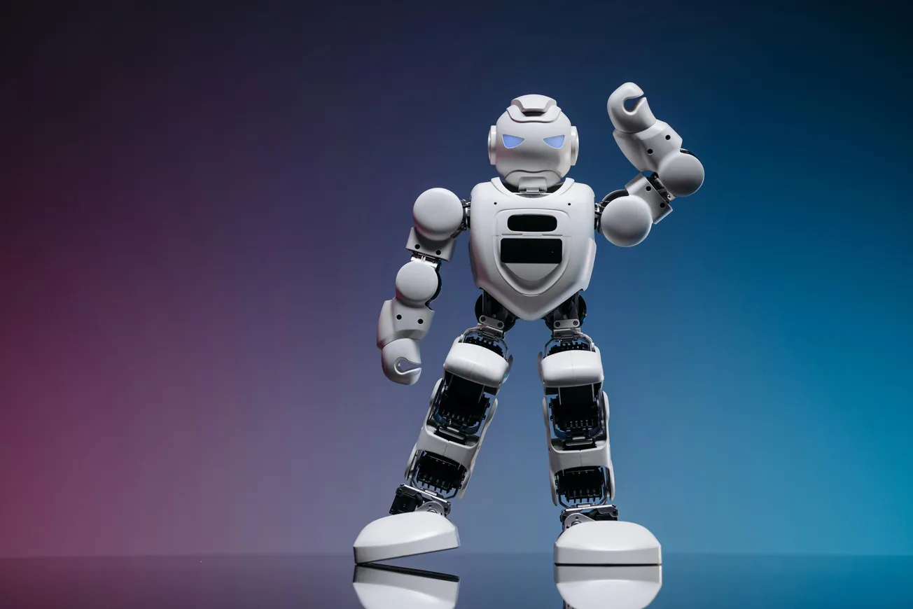 A humanoid robot with white armor stands confidently against a gradient background of purple and blue, raising a clenched fist. The mood is futuristic.