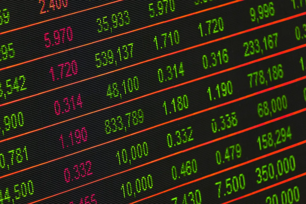 Digital stock market display with rows of numbers in red and green. The screen suggests financial data, with gains in green and losses in red.