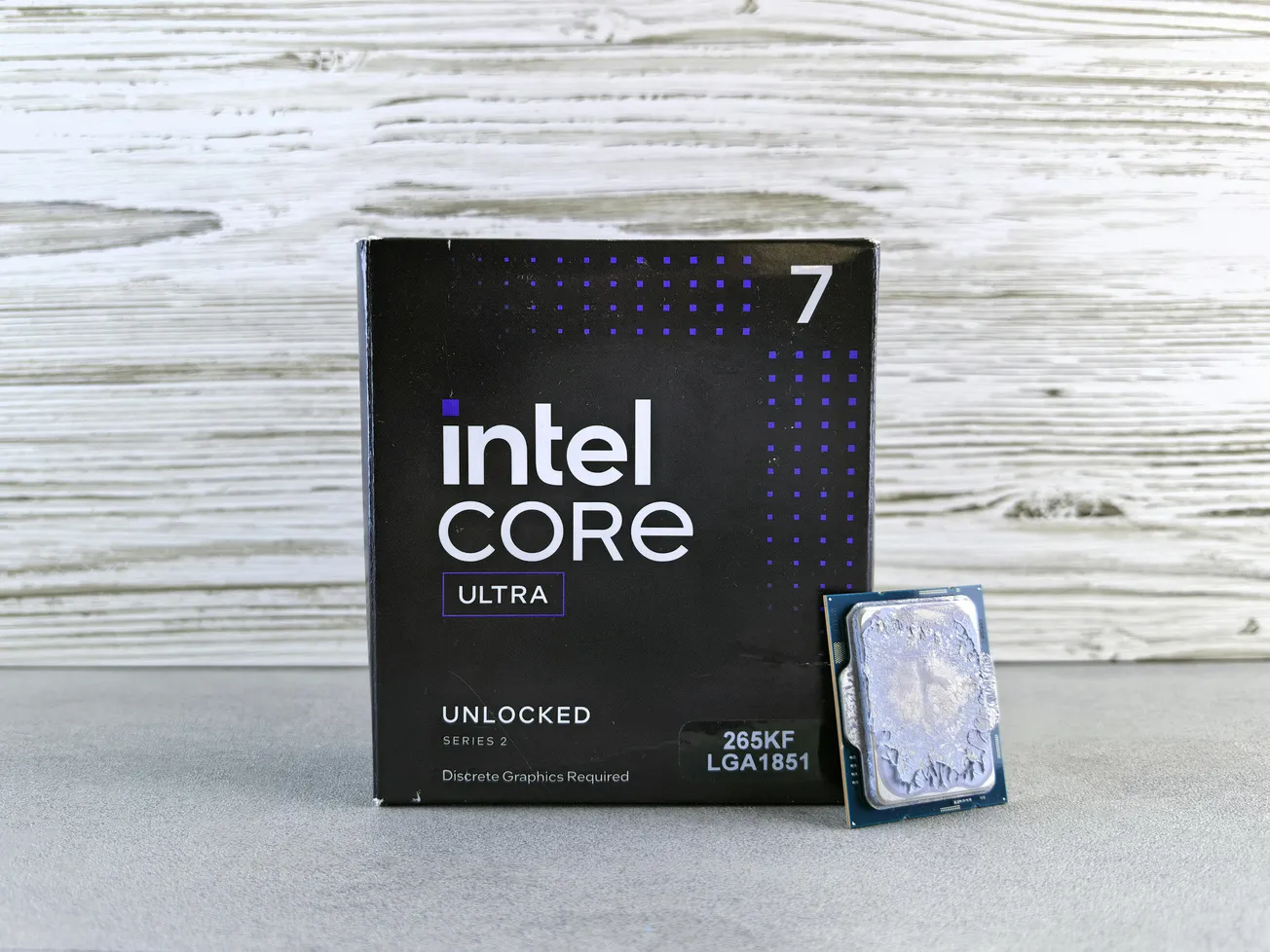 Box of Intel Core Ultra 7 Processor with model 265KF LGA1851, placed on a wooden background. The processor is displayed alongside the box.