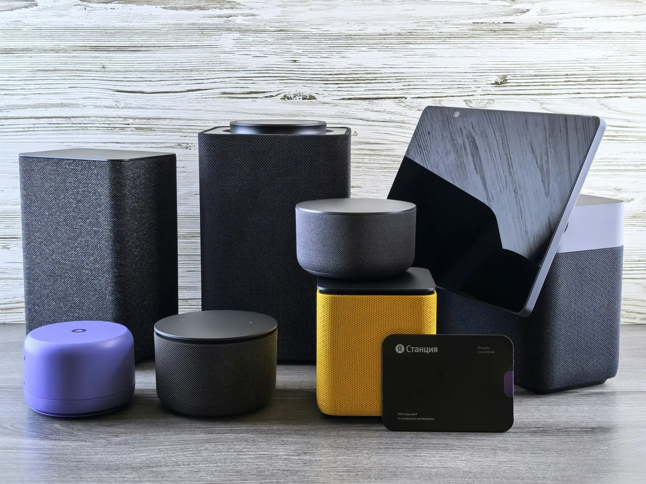 A collection of smart speakers and devices, including cylindrical and square shapes in black and yellow on a wood-textured background. Modern tech vibe.