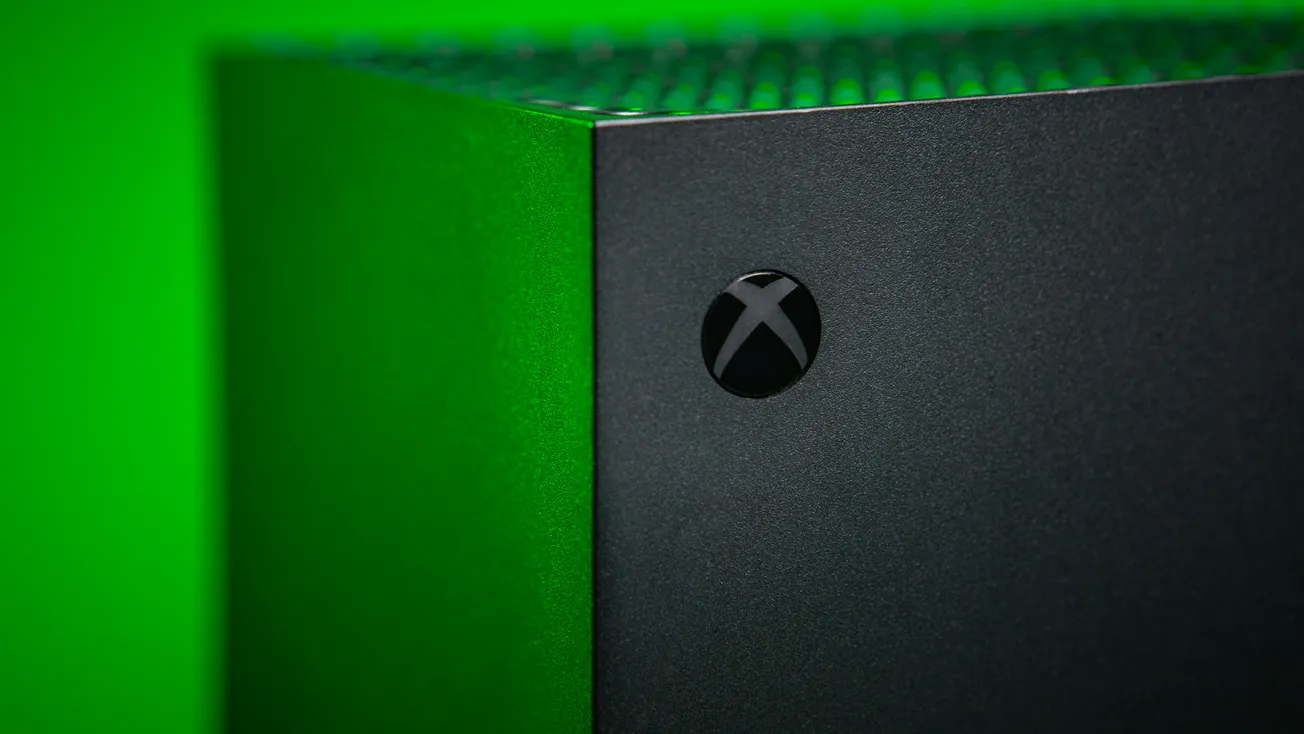 Close-up of a black Xbox console against a vibrant green background. The Xbox logo is visible on the front, highlighting a sleek, modern design.